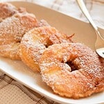Close-up of fried donuts dusted with powdered sugar on a white plate.