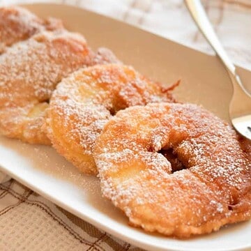 Close-up of fried donuts dusted with powdered sugar on a white plate.