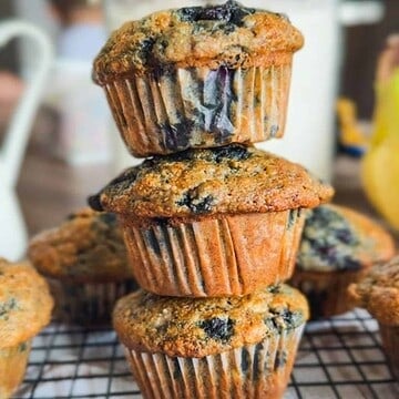 Stack of blueberry muffins on cooling rack with blueberries inside.