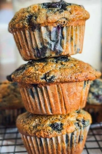 Stack of blueberry muffins on cooling rack with blueberries inside.