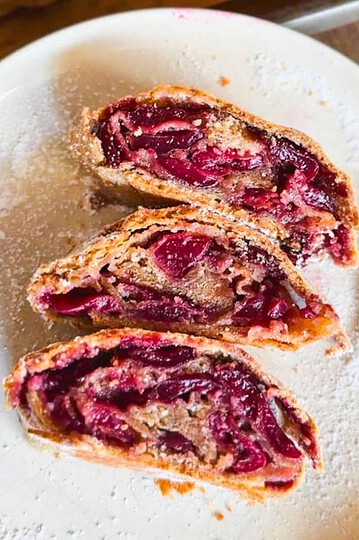Close-up of cherry pie slices on a white plate with a fork.