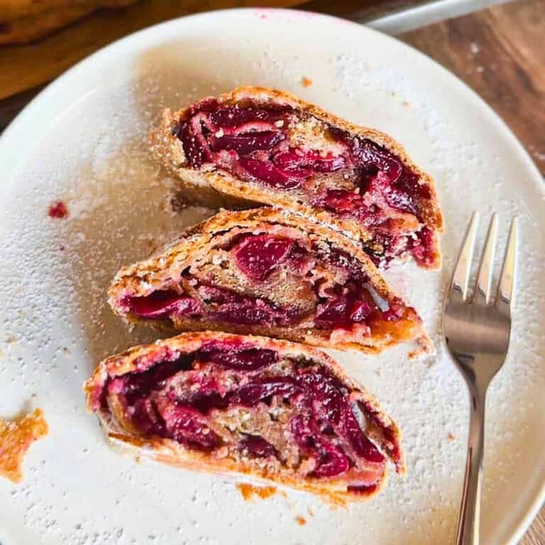Close-up of cherry pie slices on a white plate with a fork.
