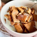 Close-up of crispy French toast sticks with syrup in a white bowl.