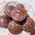 Delicious chocolate muffins topped with chocolate chips on a white cloth.