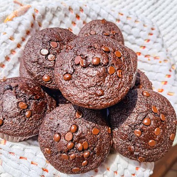 Delicious chocolate muffins topped with chocolate chips on a white cloth.