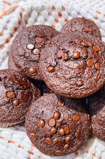 Delicious chocolate muffins topped with chocolate chips on a white cloth.