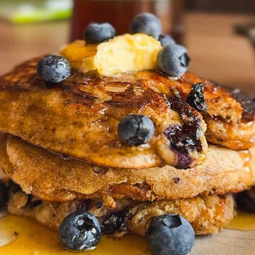 Stack of blueberry pancakes topped with butter, blueberries, and syrup.