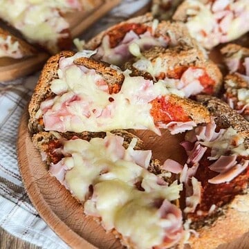 Close-up of cheesy ham bagel bites with melted cheese and ham slices.