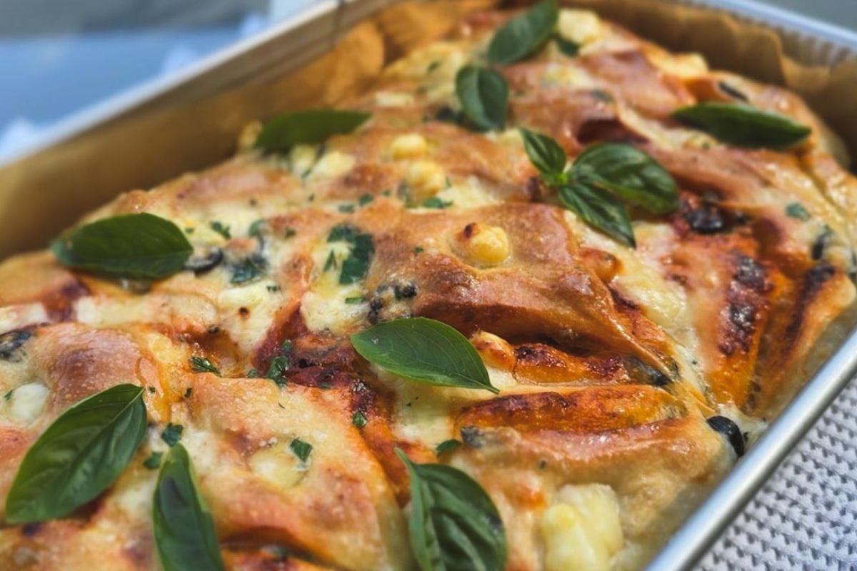 Close-up of sourdough focaccia with tomatoes, pesto, olives, and fresh basil.