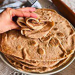 Stack of freshly baked flatbreads with a hand lifting one.