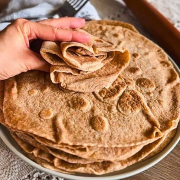 Stack of freshly baked flatbreads with a hand lifting one.