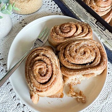 Freshly baked cinnamon rolls with sugar on top on a white plate.