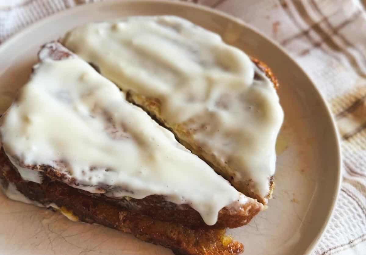 Close-up of a cinnamon roll with white icing on a plate.