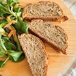 Close-up of three slices of banana nut bread on a wooden cutting board with a side salad.