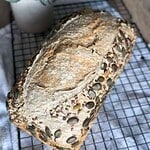 Freshly baked sourdough bread with pumpkin seeds cooling on a wire rack.