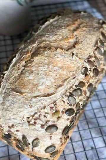 Freshly baked sourdough bread with pumpkin seeds cooling on a wire rack.