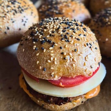 Close-up of a seeded bread roll with tomato, cheese, and filling.