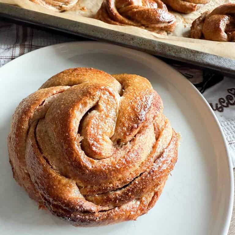 Close-up of a freshly baked cinnamon roll on a white plate.