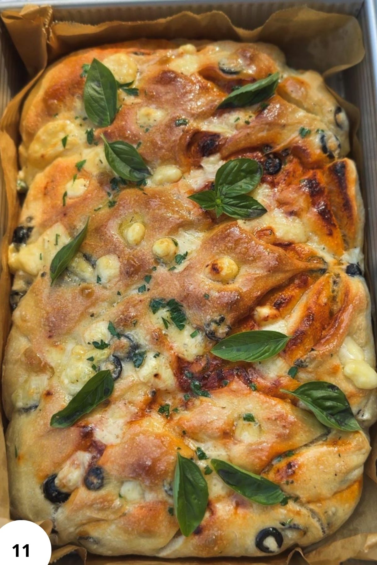 Close-up of sourdough focaccia with tomatoes, olives, pesto, and fresh basil.