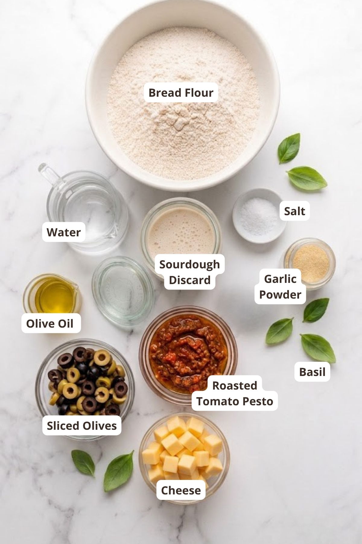 Ingredients for sourdough tomato pesto focaccia including bread flour, olives, cheese, and basil.