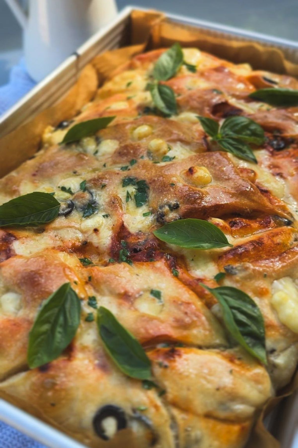 Close-up of sourdough focaccia with tomatoes, pesto, olives, and basil leaves.