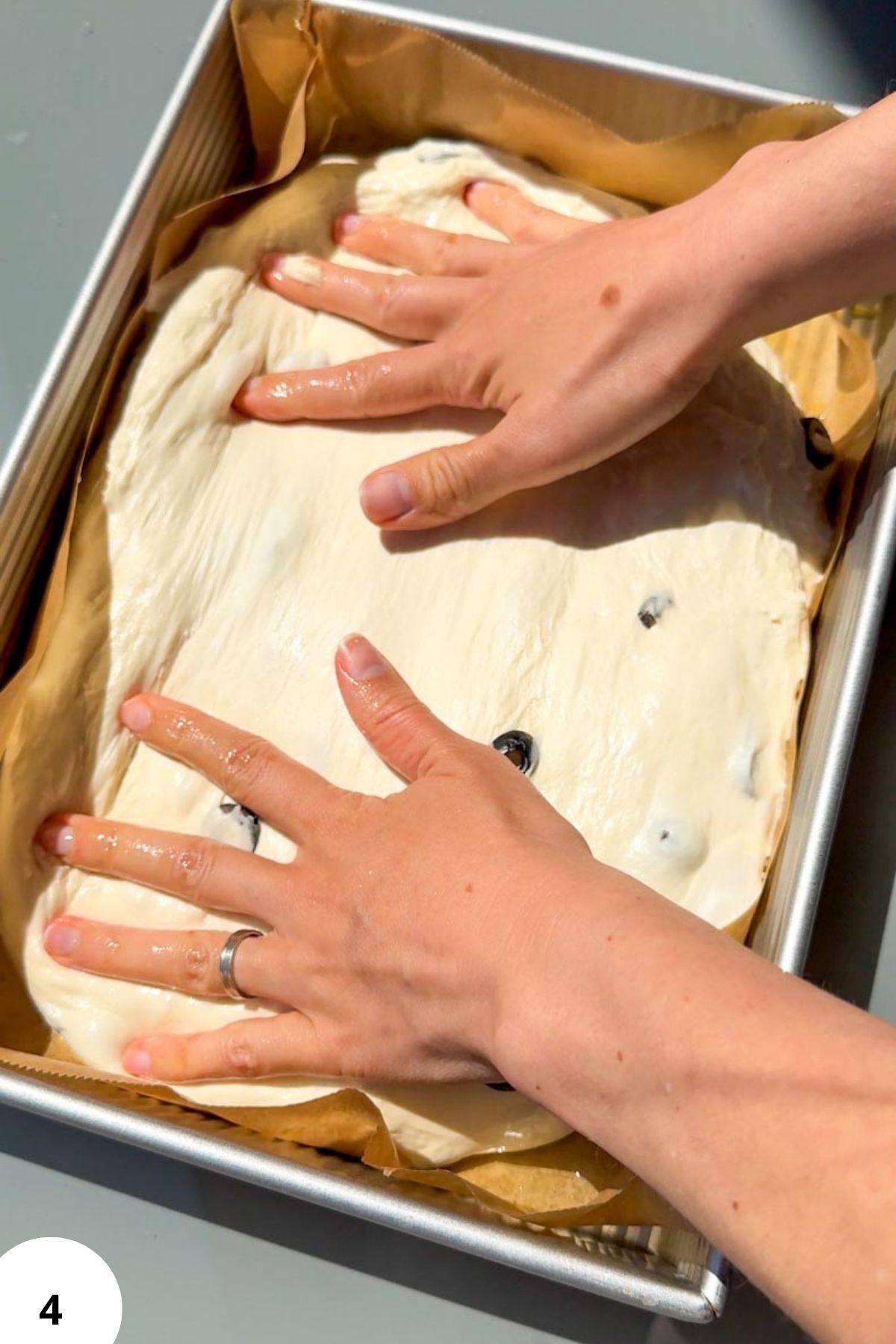 Hands performing stretch and fold technique on sourdough dough in a baking tray.
