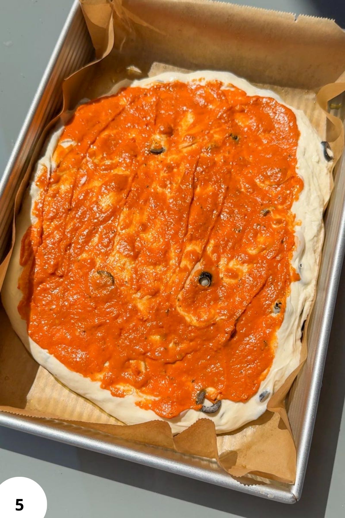 Fresh sourdough focaccia topped with vibrant tomato pesto and black olives.