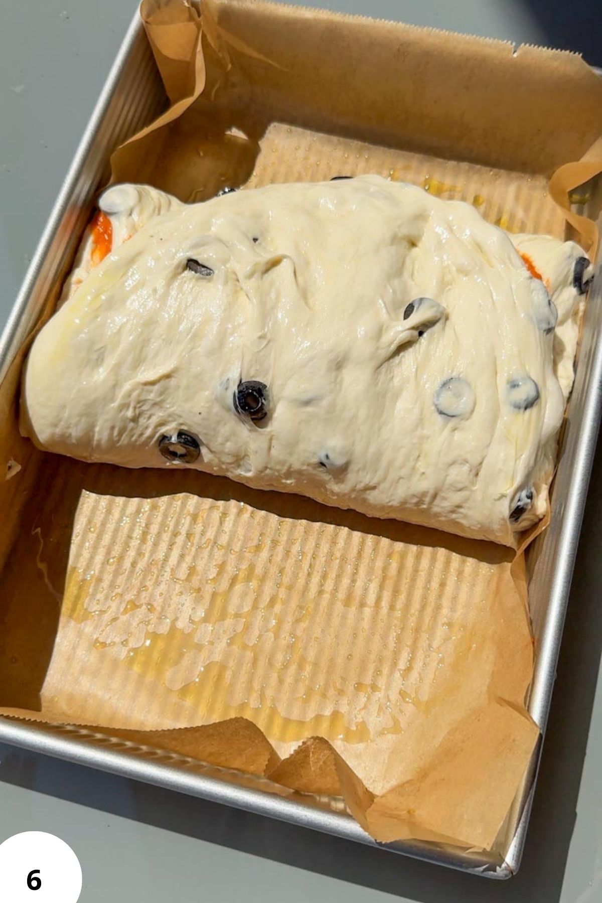 Fresh sourdough bread dough with olives in a baking pan.
