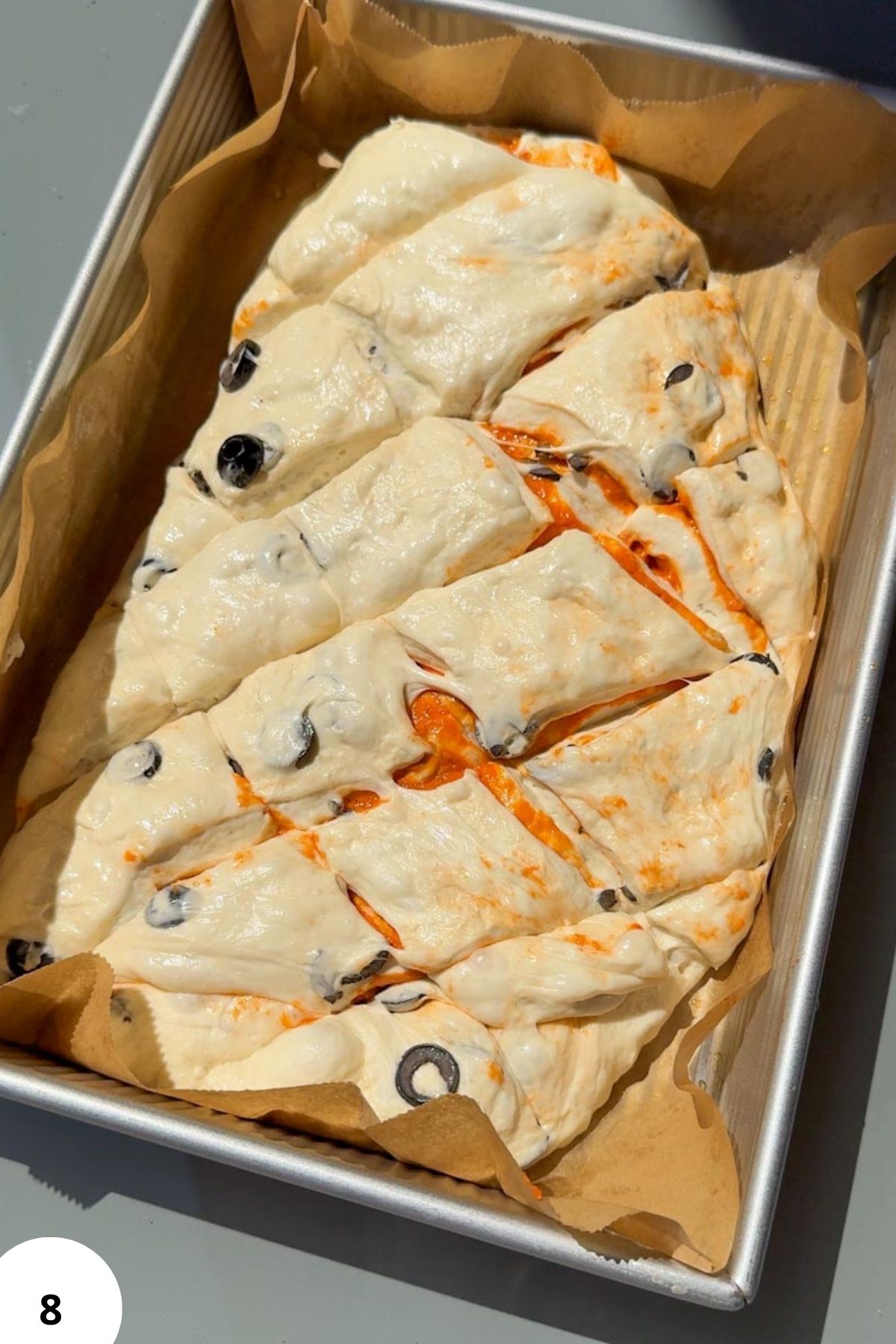 Fresh sourdough focaccia topped with olives and tomato slices in a baking tray.