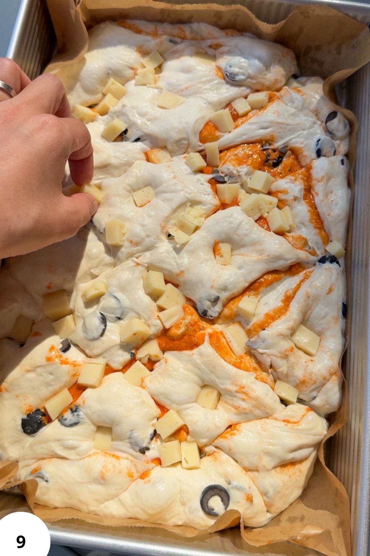 Preparing sourdough focaccia with cheese, tomatoes, and olives for baking.