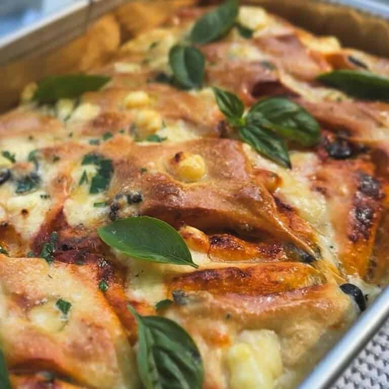 Close-up of sourdough focaccia with tomatoes, pesto, olives, and basil.