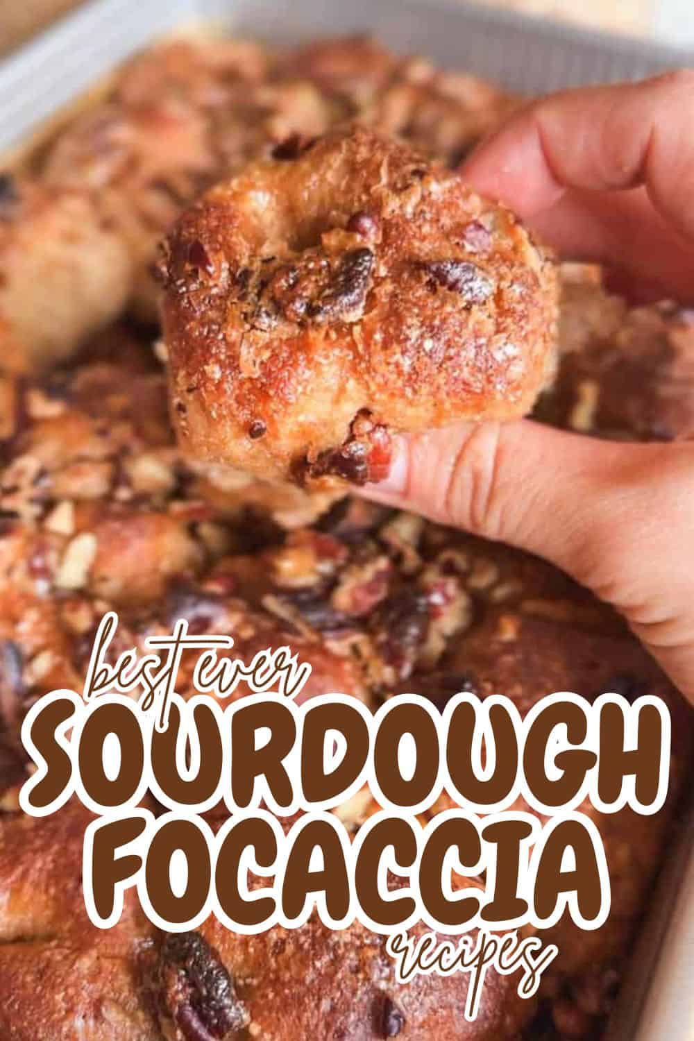 Close-up of a hand holding a piece of sourdough focaccia bread with toppings.