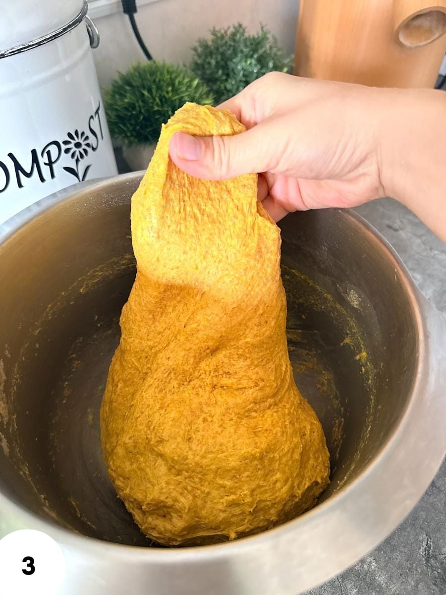 Hand stretching dough in a mixing bowl for bread baking.