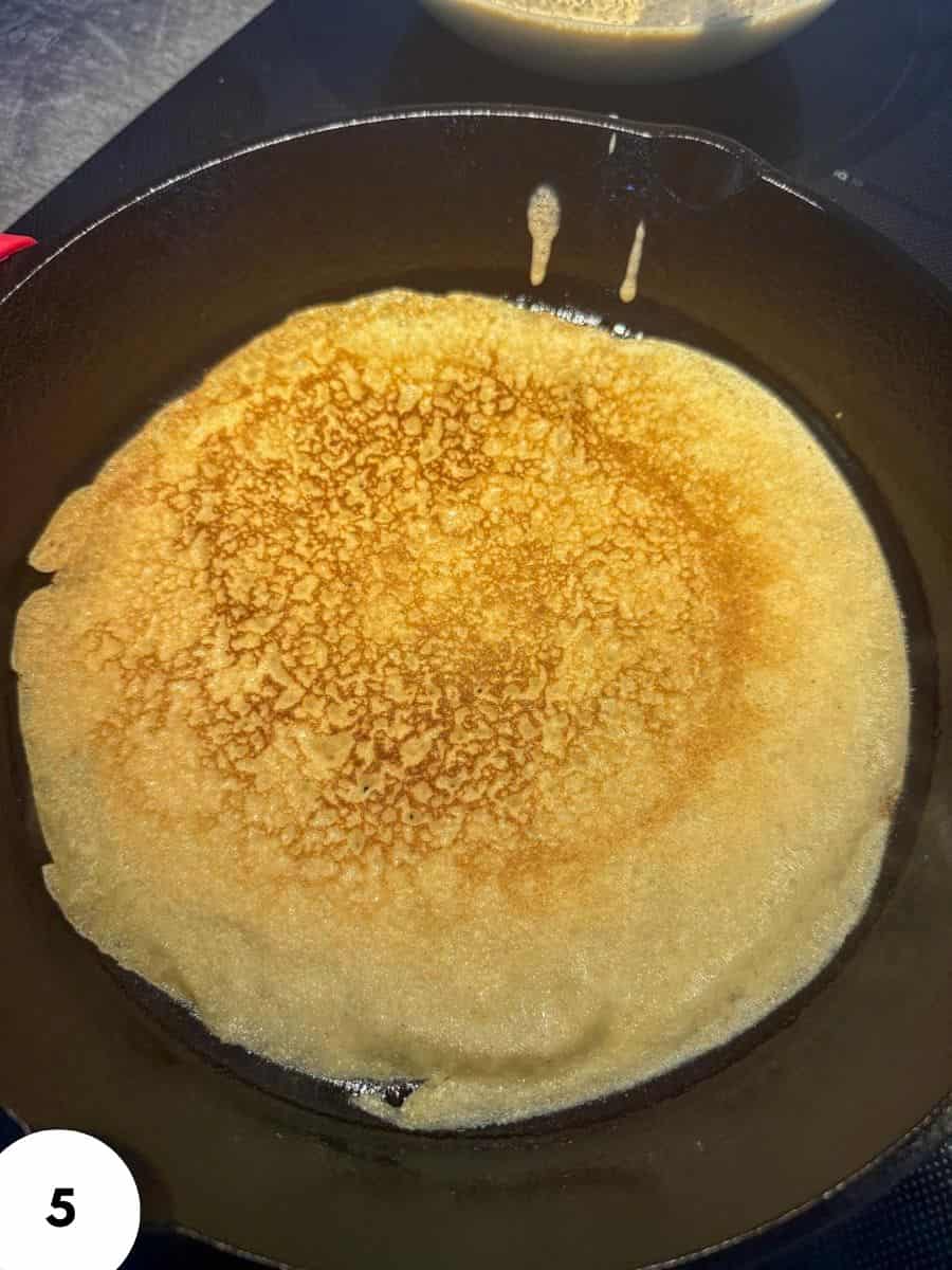 Golden crepe cooking in a black skillet for bread making.