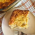Freshly baked cornbread slice on a white plate with a fork.