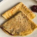 Close-up of golden-brown crepes with fruit filling on a plate.