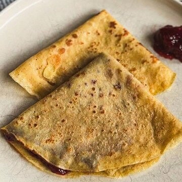 Close-up of golden-brown crepes with fruit filling on a plate.