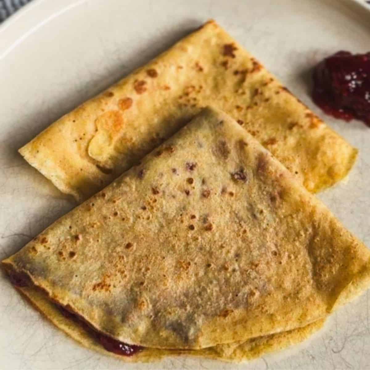 Close-up of golden-brown crepes with fruit filling on a plate.