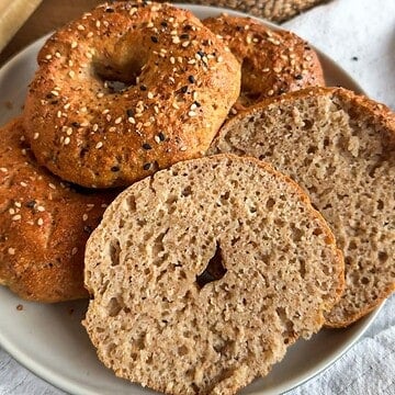 Freshly baked bagels with sesame seeds on top, sliced to show soft interior.