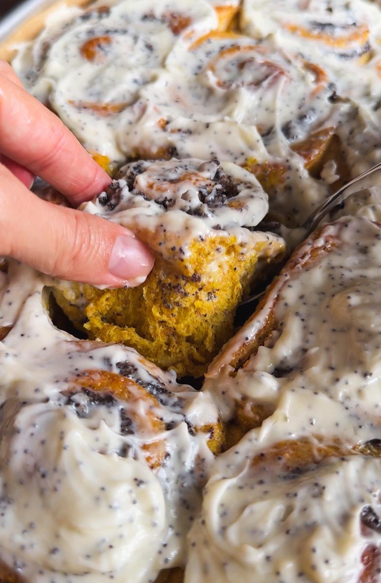 Close-up of cinnamon rolls with creamy frosting and a hand holding a piece.