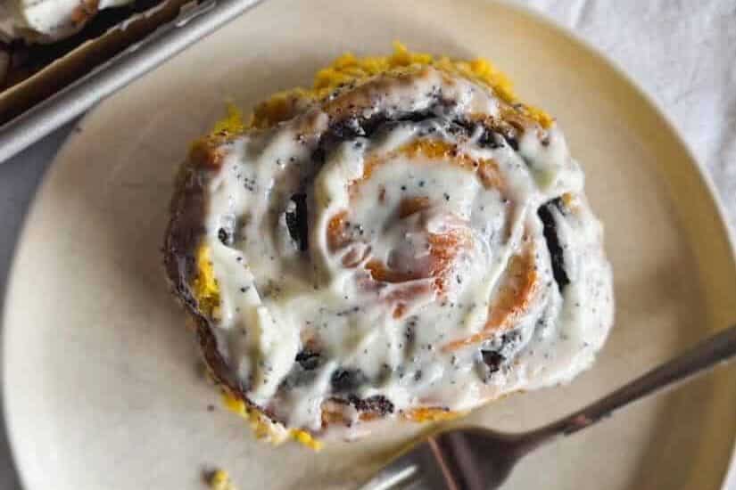 Close-up of freshly baked cinnamon rolls with creamy frosting on a white plate.