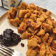 Close-up of crispy chicken pieces with cranberry sauce on a white plate.