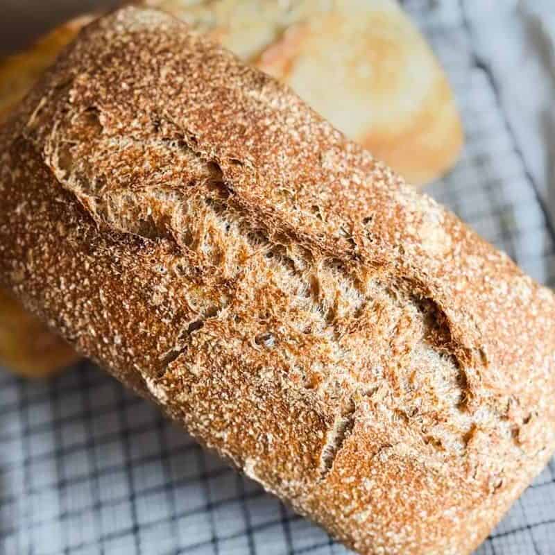 Crusty sourdough loaf with a golden-brown crust on a cooling rack.