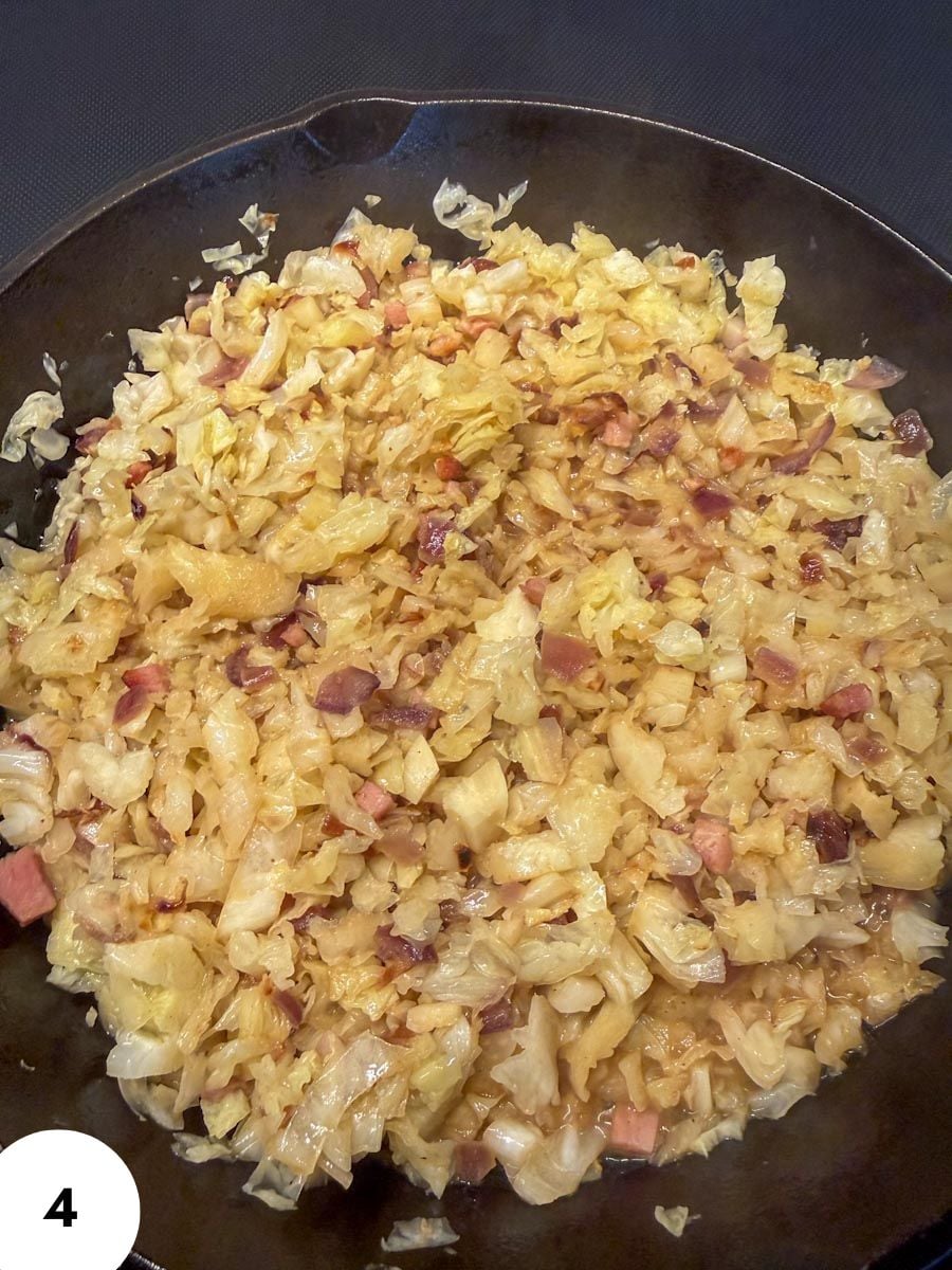 Stir-fried cabbage with ham in a black skillet, close-up view.