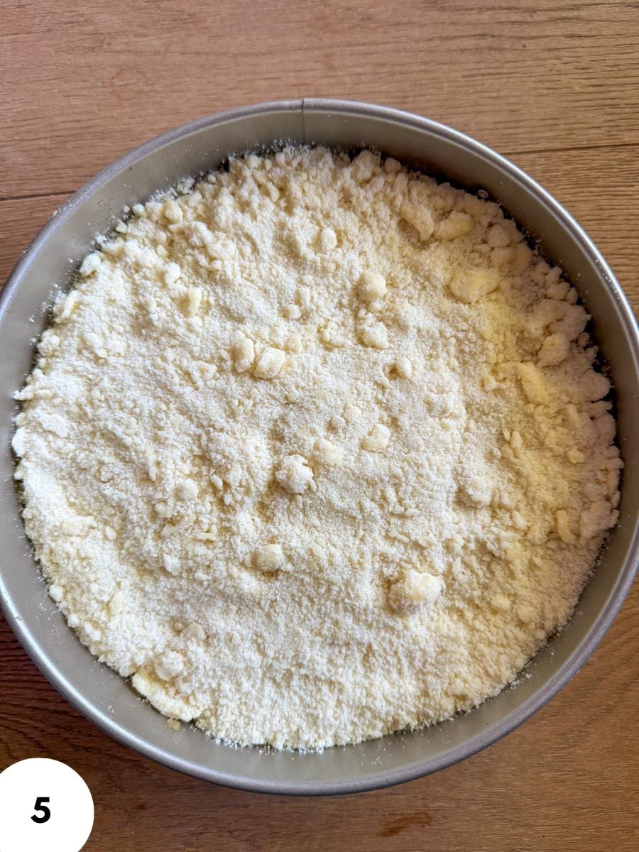 Unbaked dough with flour in a round metal bowl on wooden surface.