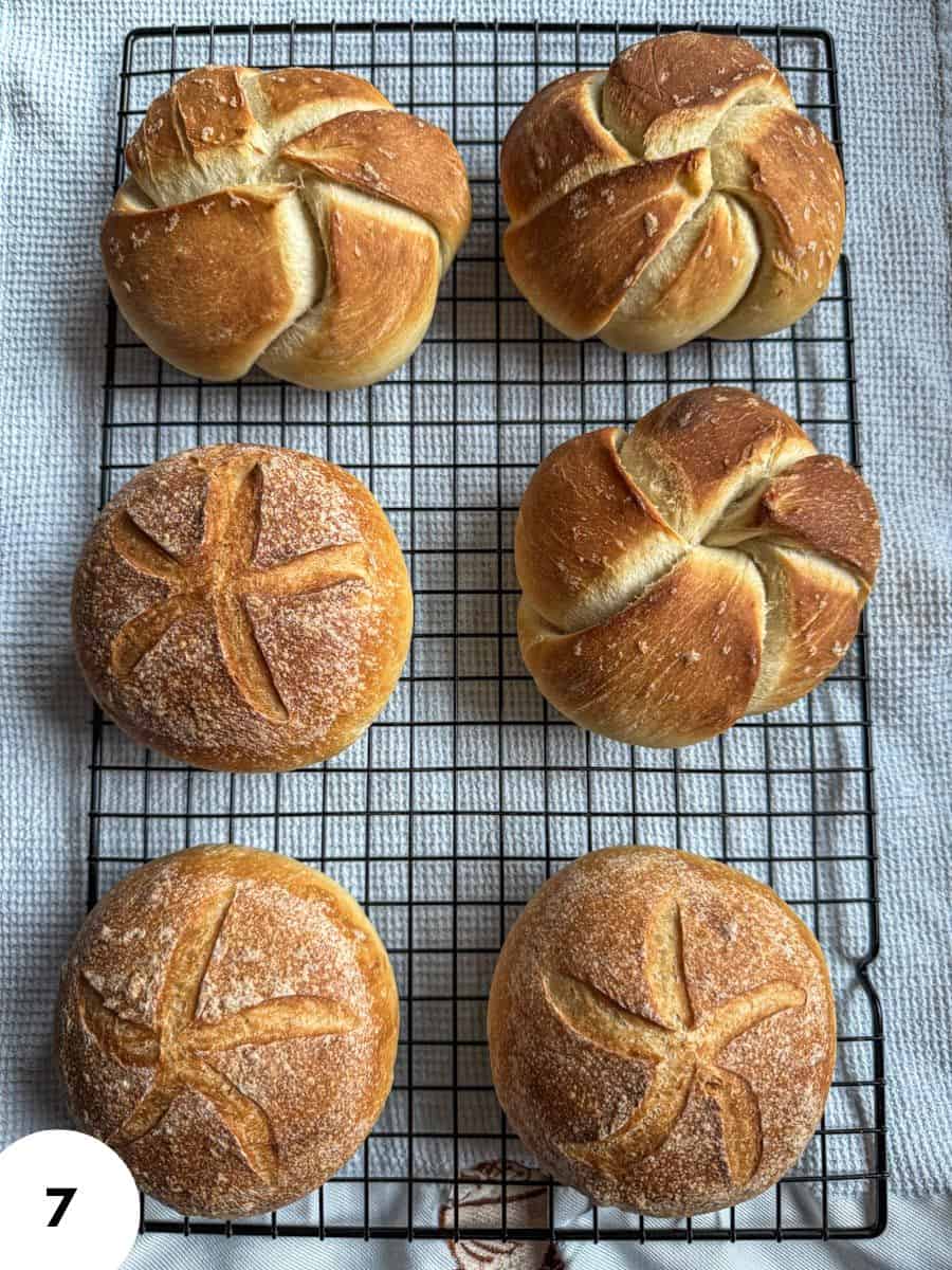 Six golden brown rolled buns cooling on a wire rack.