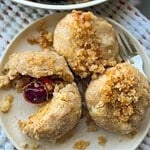 Close-up of cherry dumplings with crumble topping on a white plate.