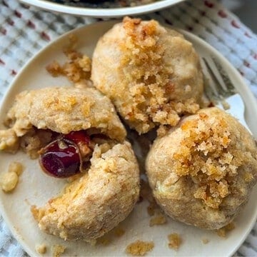 Close-up of cherry dumplings with crumble topping on a white plate.