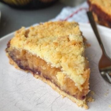 Close-up of a slice of homemade fruit pie with crumble topping on a white plate.