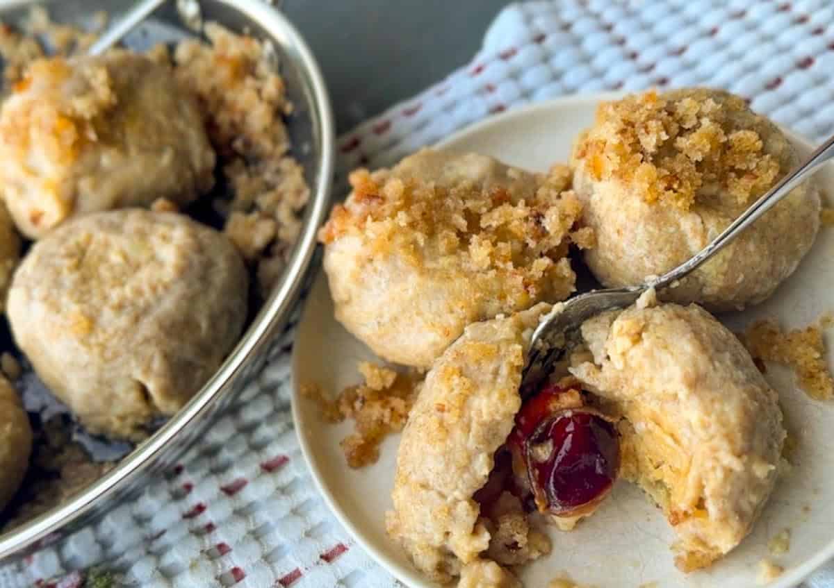 Close-up of cherry-filled dumplings with crumb topping on a white plate.